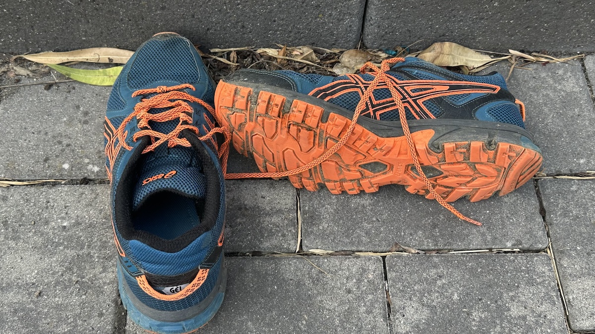 Bild für Blogbeitrag: Mein erster Lauf nach 22 Jahren Blau-orangene Laufschuhe nach dem Ausziehen auf laubbedecktem Pflasterboden.