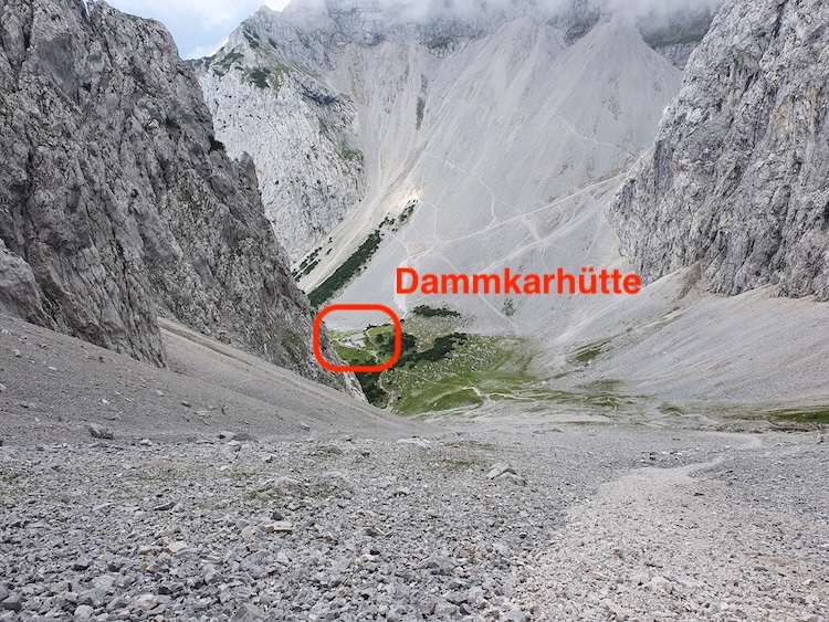 Panoramablick ins Karwendelgebirge mit der Dammkarhütte bei Mittenwald, aufgenommen aus dem oberen Dammkar. Die kleine Berghütte liegt eingebettet zwischen steilen Felswänden – ein Etappenziel der Alpenüberquerung von Oberstdorf nach Meran.
