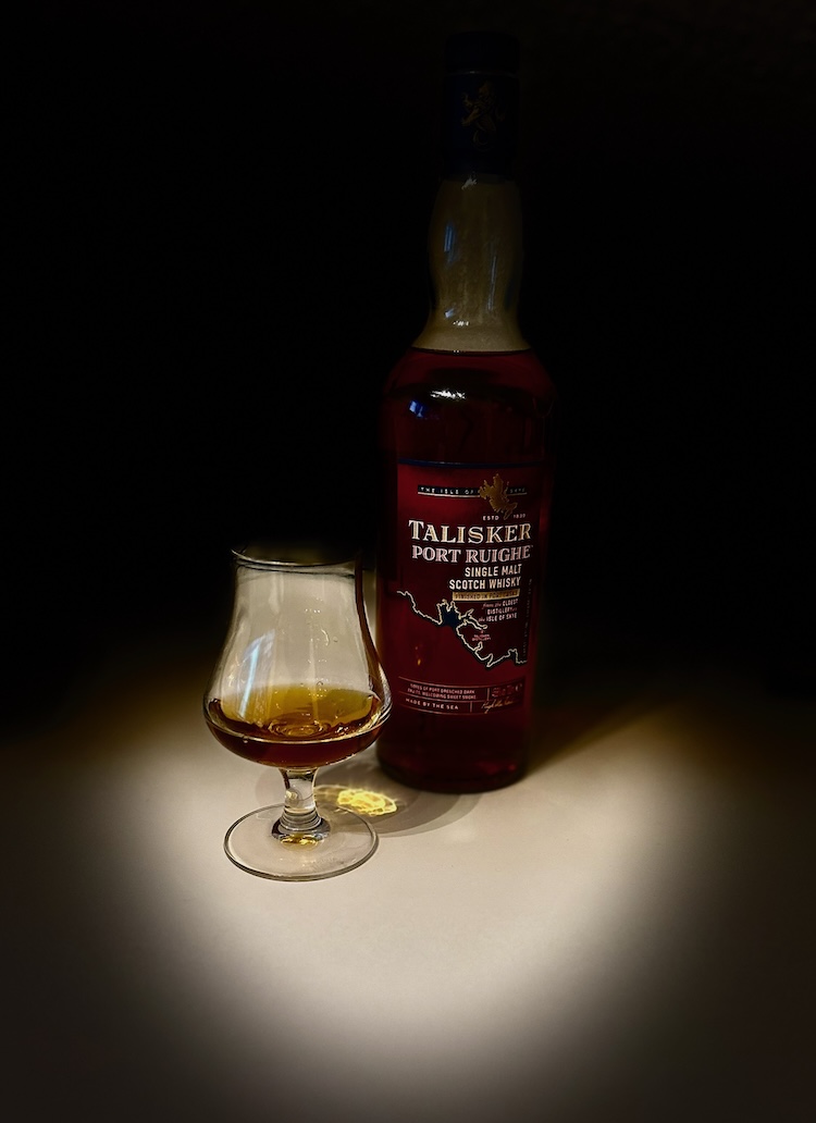 Flasche Talisker Port Ruighe Single Malt Scotch Whisky mit gefülltem Glas auf einem Tisch, stimmungsvoll beleuchtet – Symbol für Achtsamkeit, Genuss und Dankbarkeit im Leben mit Krebs.