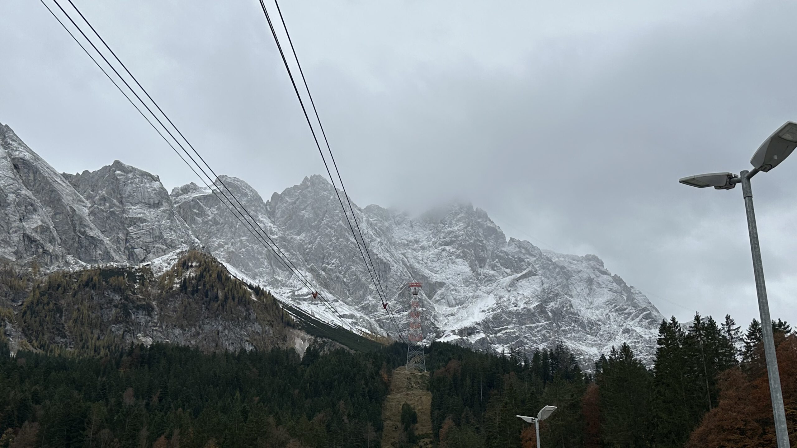 Schneebedeckte Zugspitze im Nebel mit Seilbahntrassen, aufgenommen an einem grauen Herbsttag in Bayern.