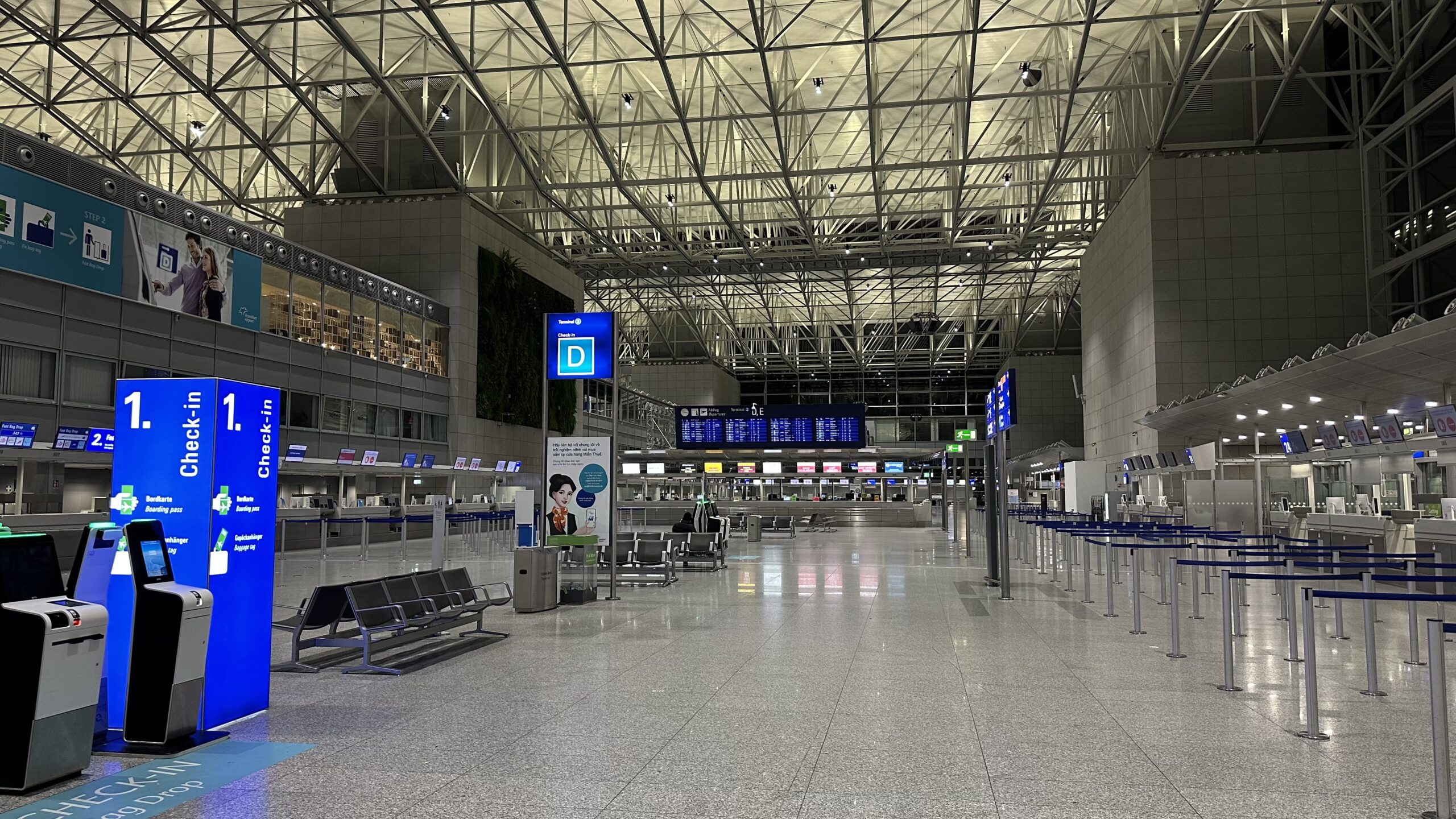 Leere, hell erleuchtete Abflughalle im Terminal 2 des Frankfurter Flughafens mit Check-in-Schaltern und Anzeigetafeln.