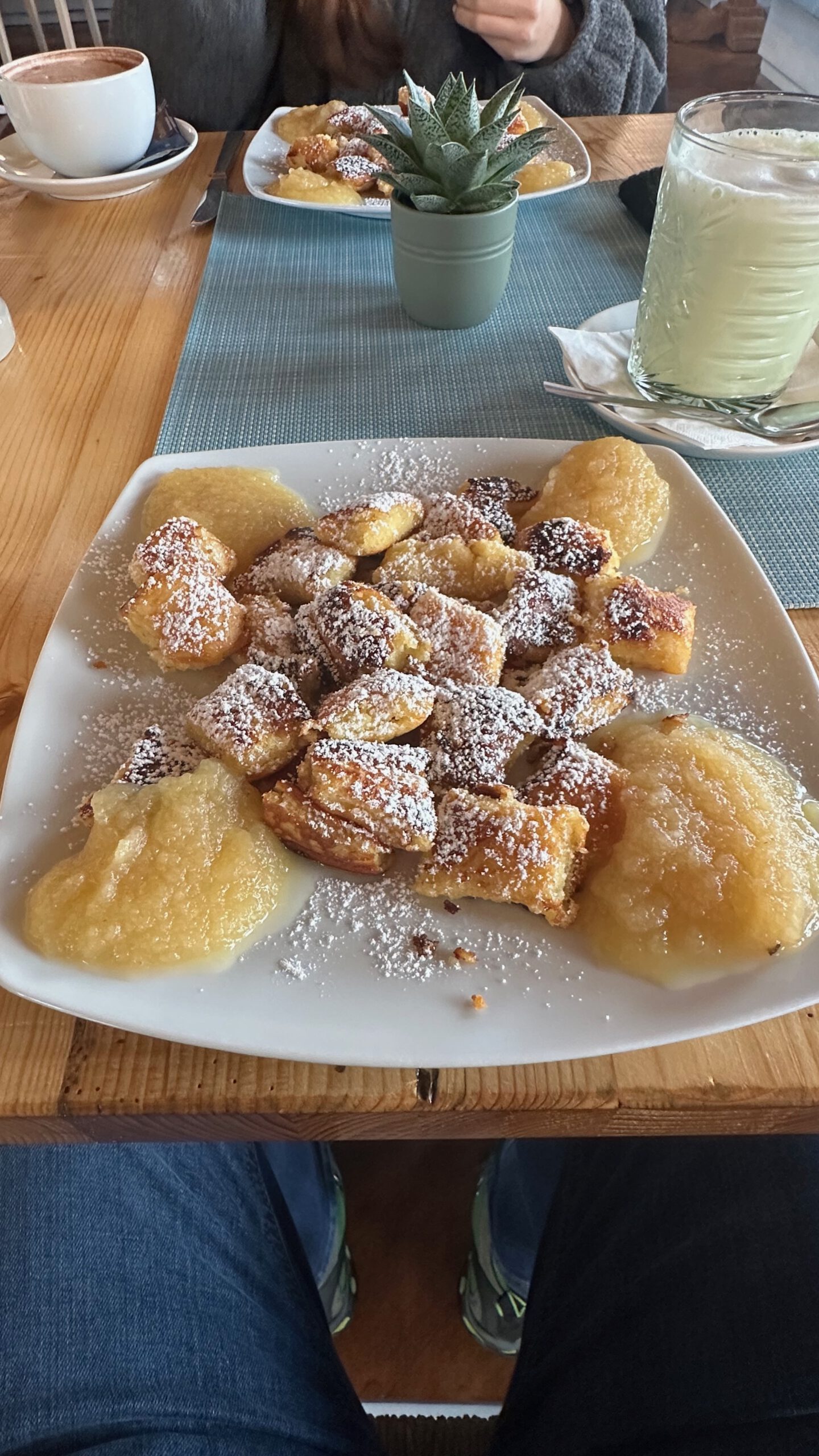 Teller mit Kaiserschmarrn und Apfelmus in einem Café, im Hintergrund eine weitere Portion und eine Tasse Heißgetränk.