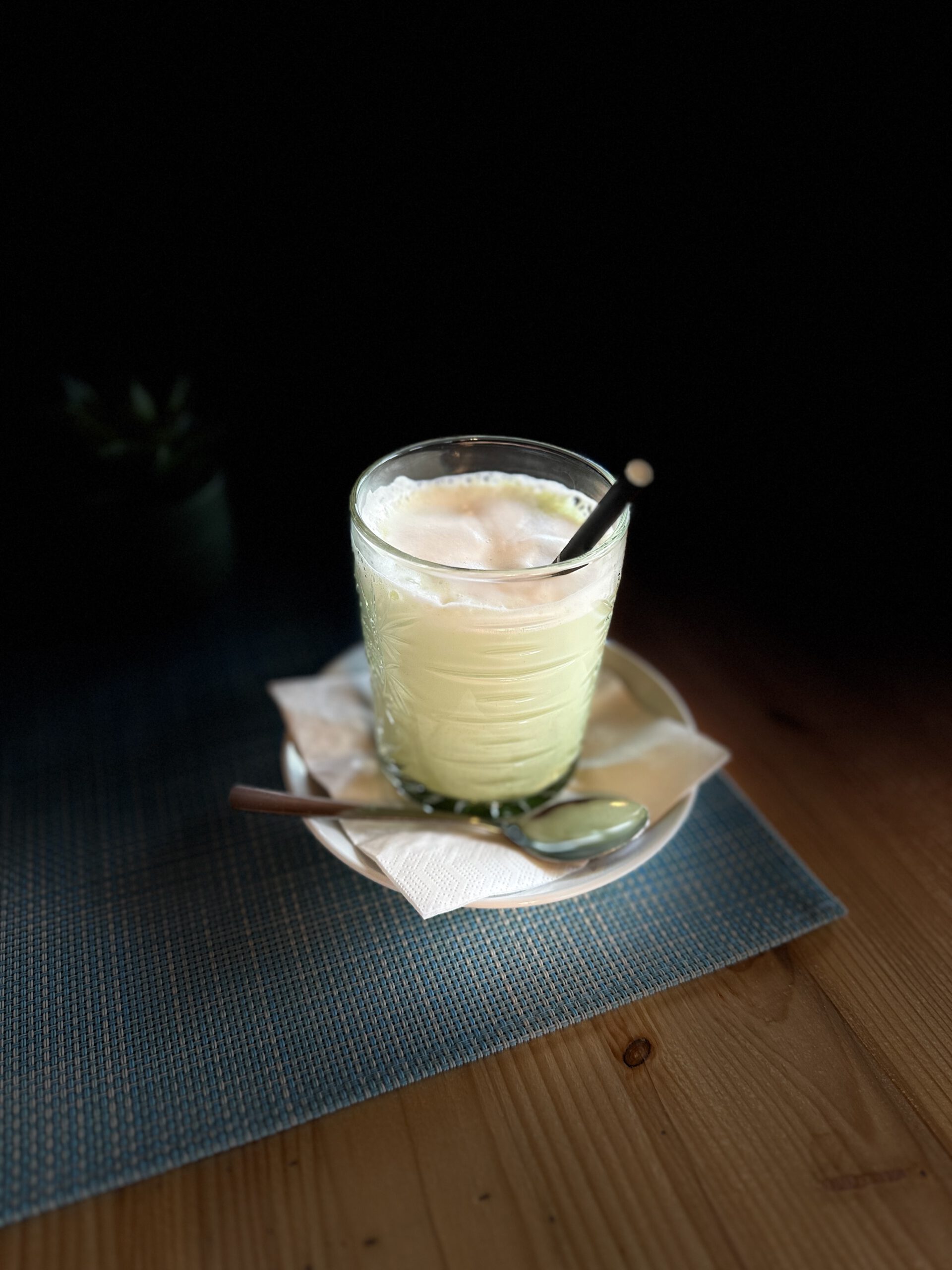 Glas mit heißem Matcha-Latte auf einem Tischset, serviert mit Löffel und Serviette in einem Café.