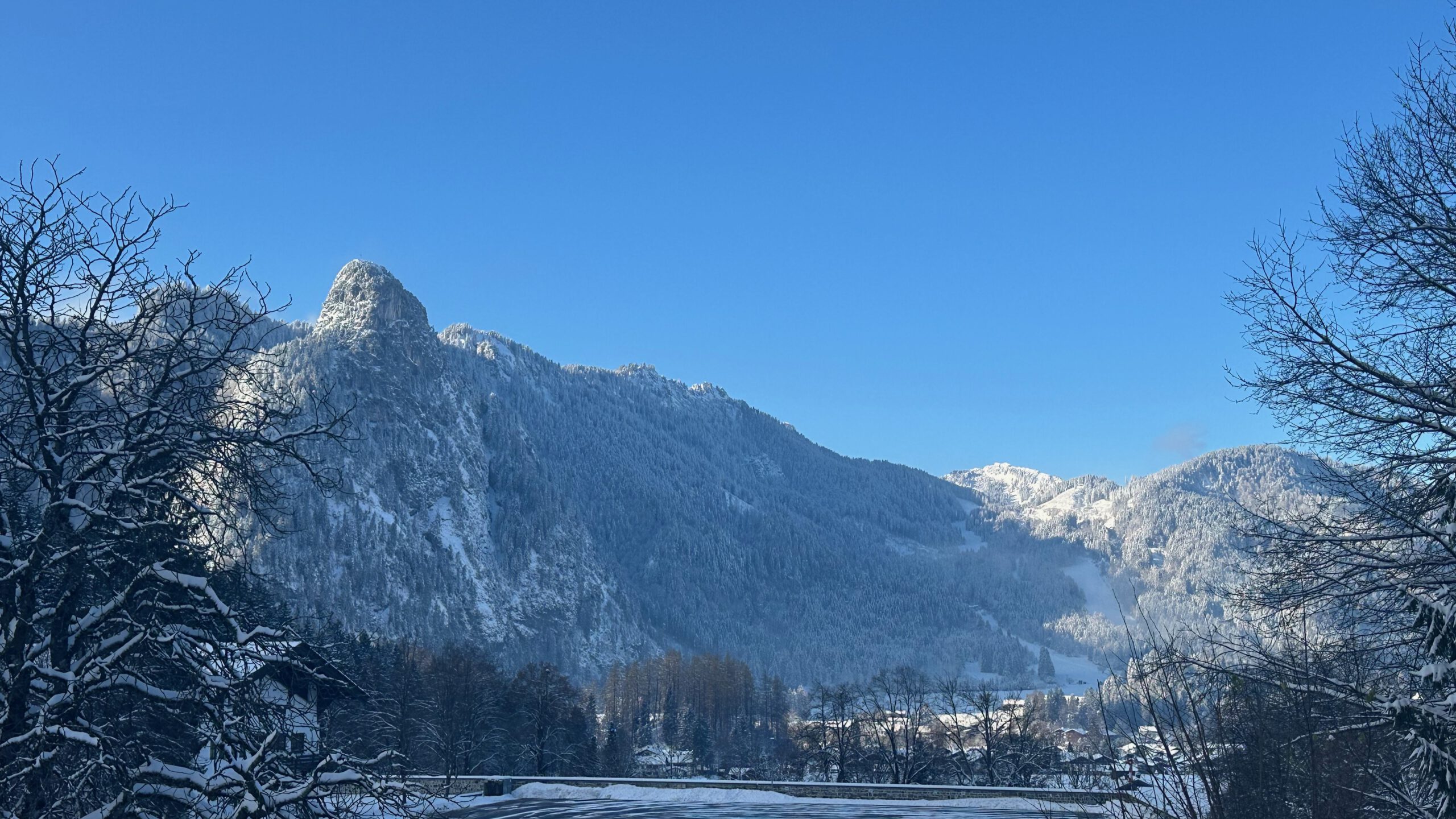 Verschneite Berglandschaft bei Oberammergau mit Blick auf den markanten Kofel; klare Sicht, blauer Himmel und schneebedeckte Bäume im Vordergrund.