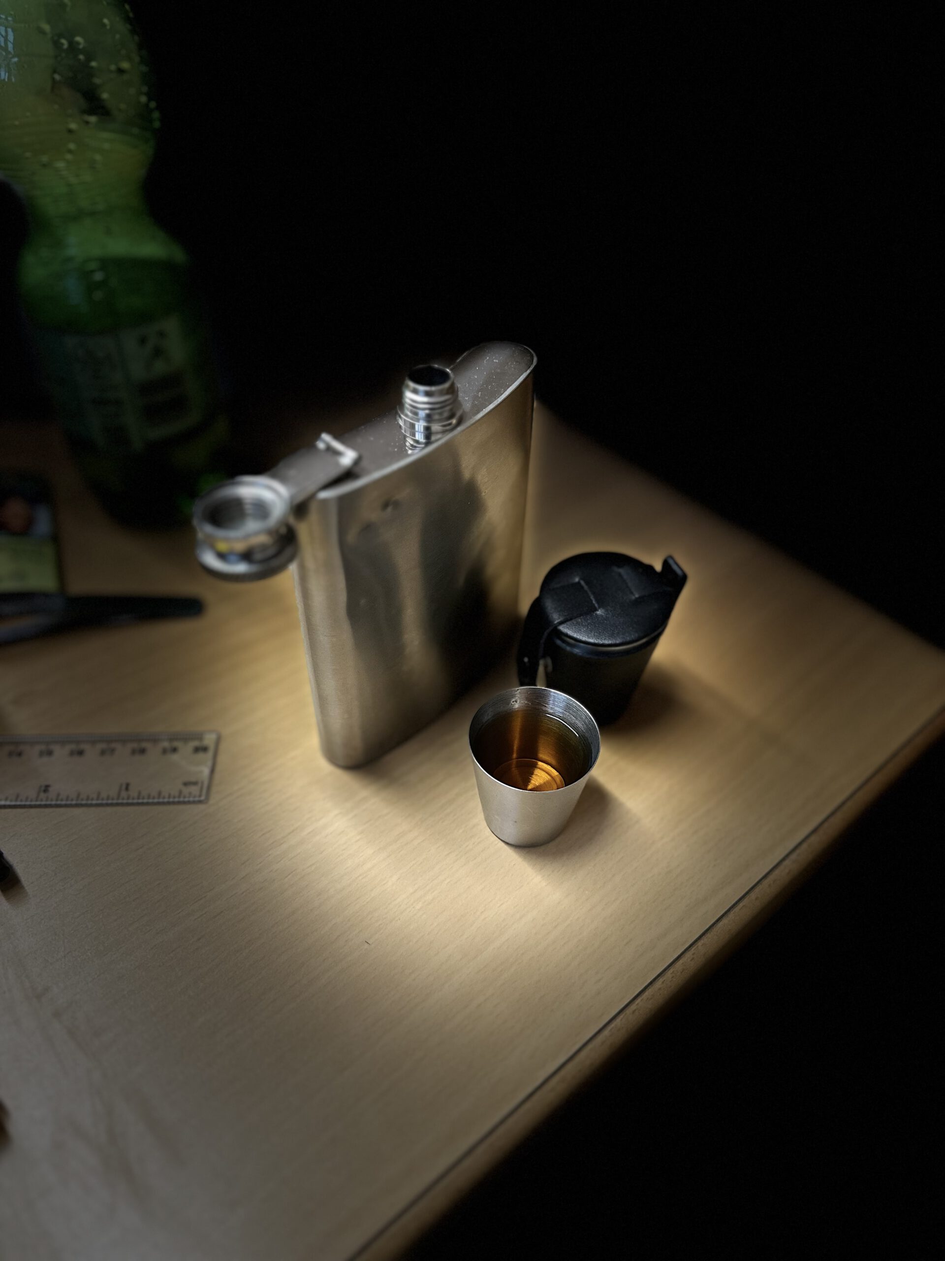 Flachmann aus Edelstahl mit eingeschenktem Single Malt Whisky in einem Metallbecher auf einem Tisch.