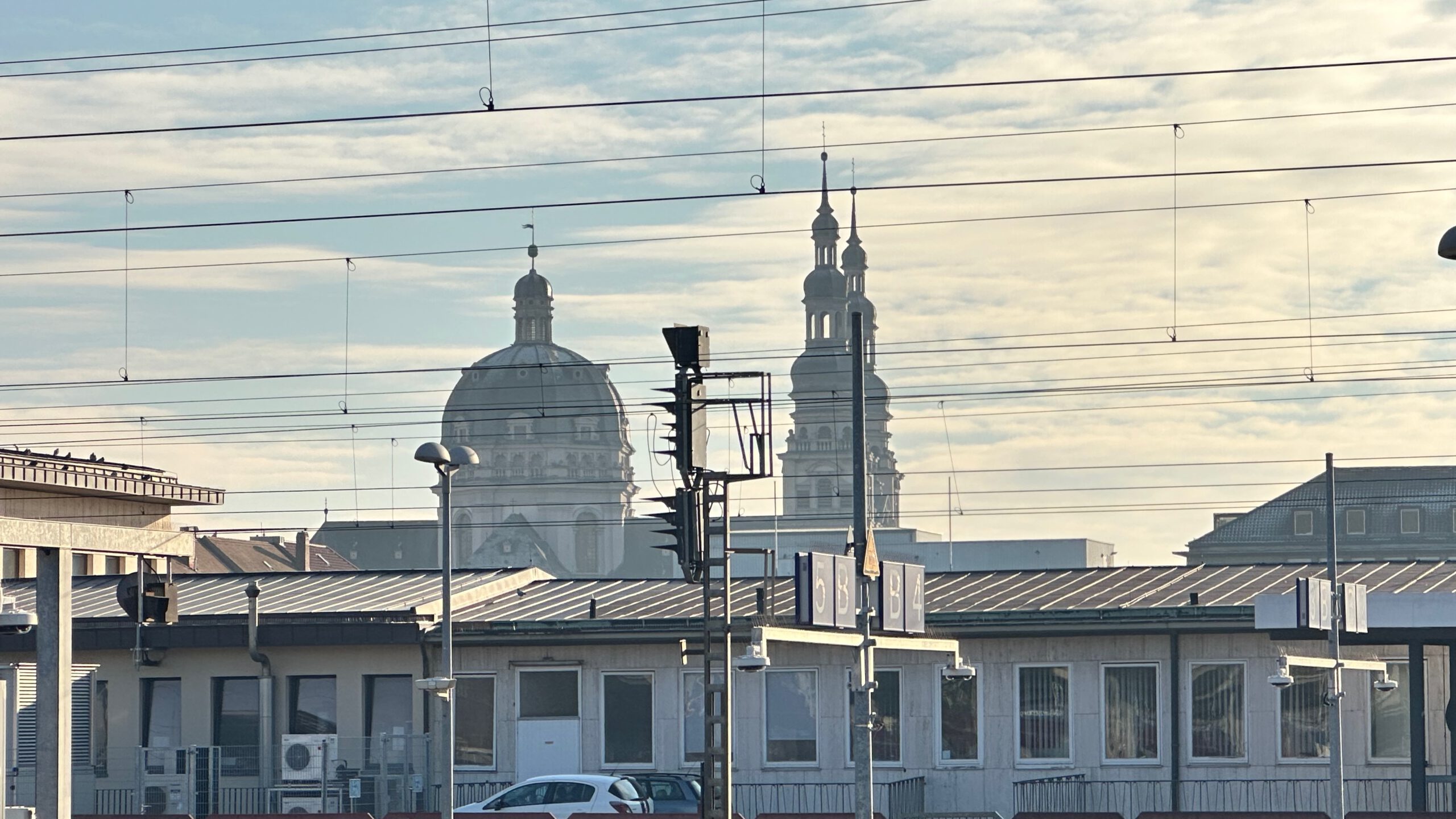 Panoramaaufnahme vom Würzburger Bahnhof aus, mit vielen Oberleitungen im Vordergrund und den markanten Kuppeln und Türmen der Stadt im Hintergrund.