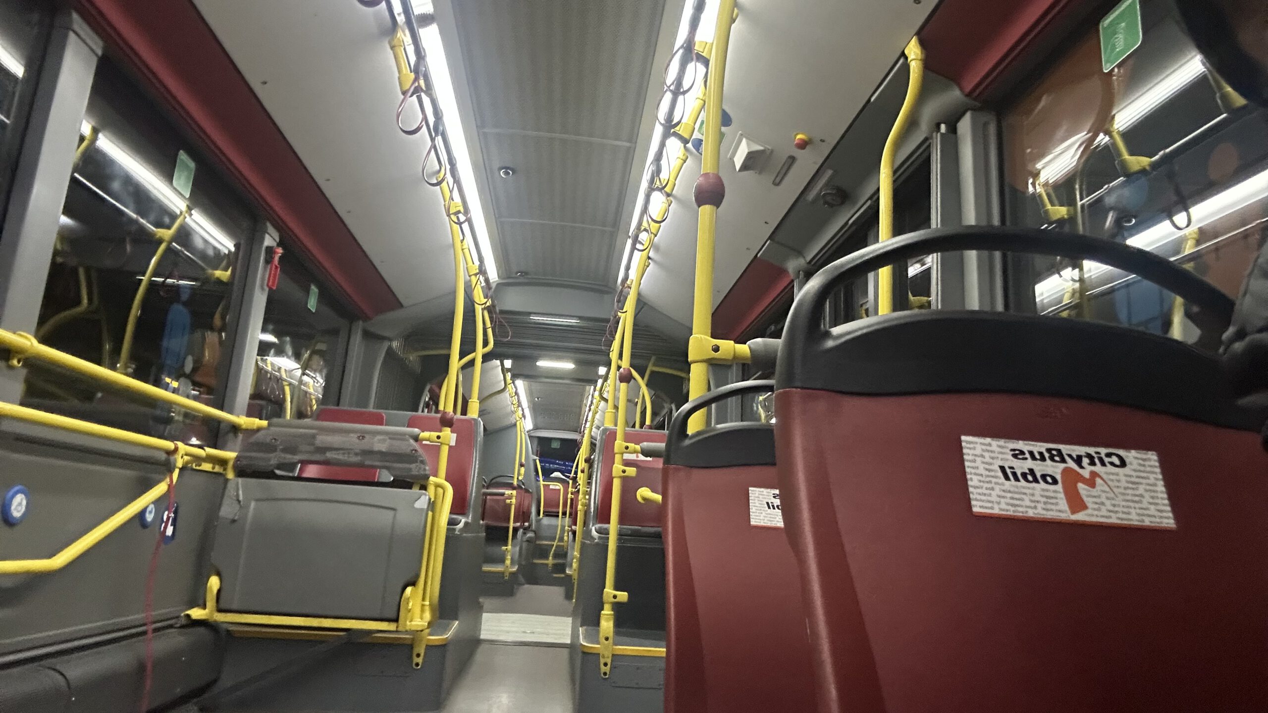 Innenraum eines leeren Shuttle-Busses am Flughafen Frankfurt mit gelben Haltestangen und roten Sitzen, der zwischen den Terminals fährt.