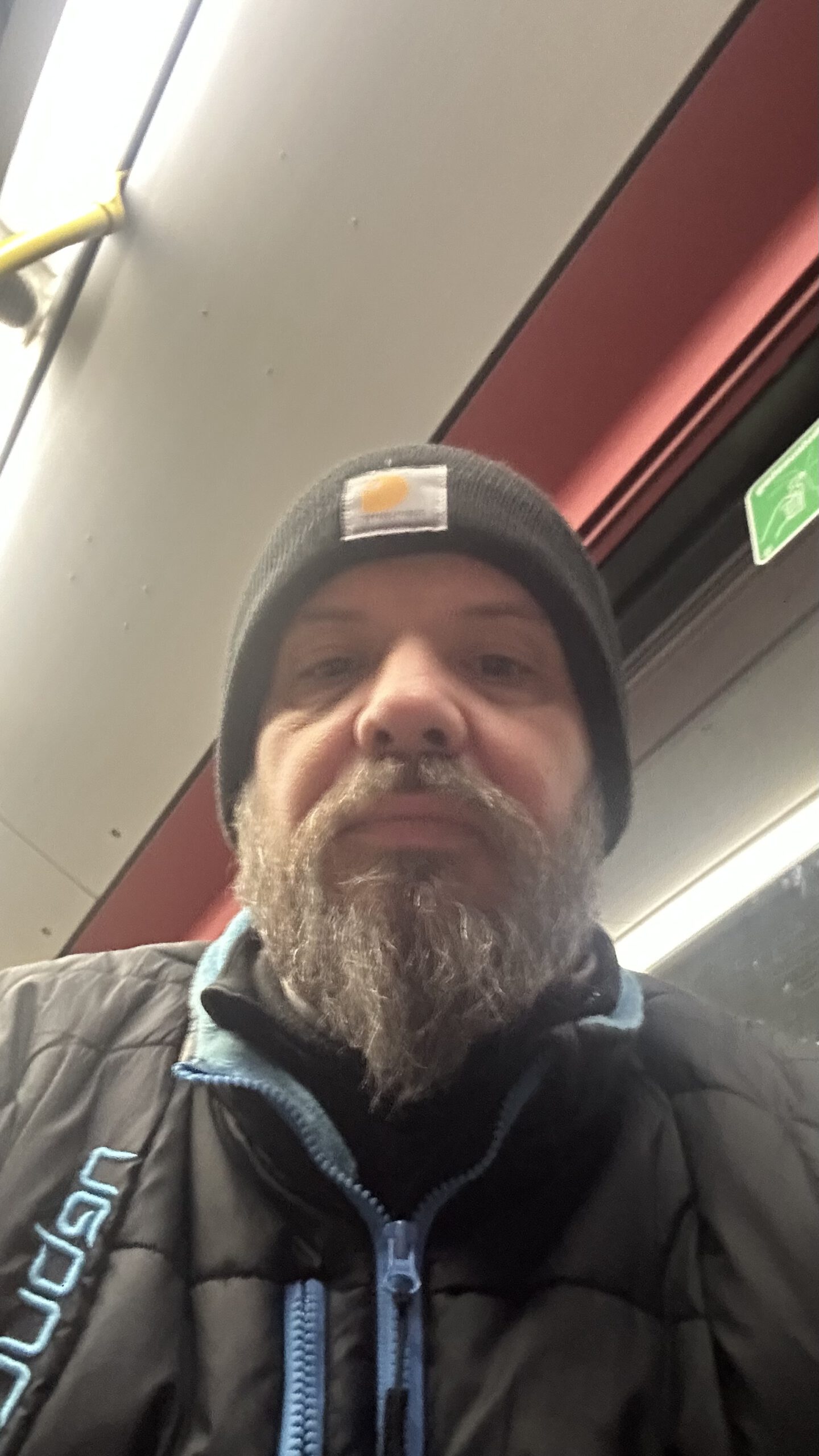 Marco sitzt frühmorgens mit Mütze und Winterjacke im Shuttle-Bus zwischen den Terminals am Flughafen Frankfurt.