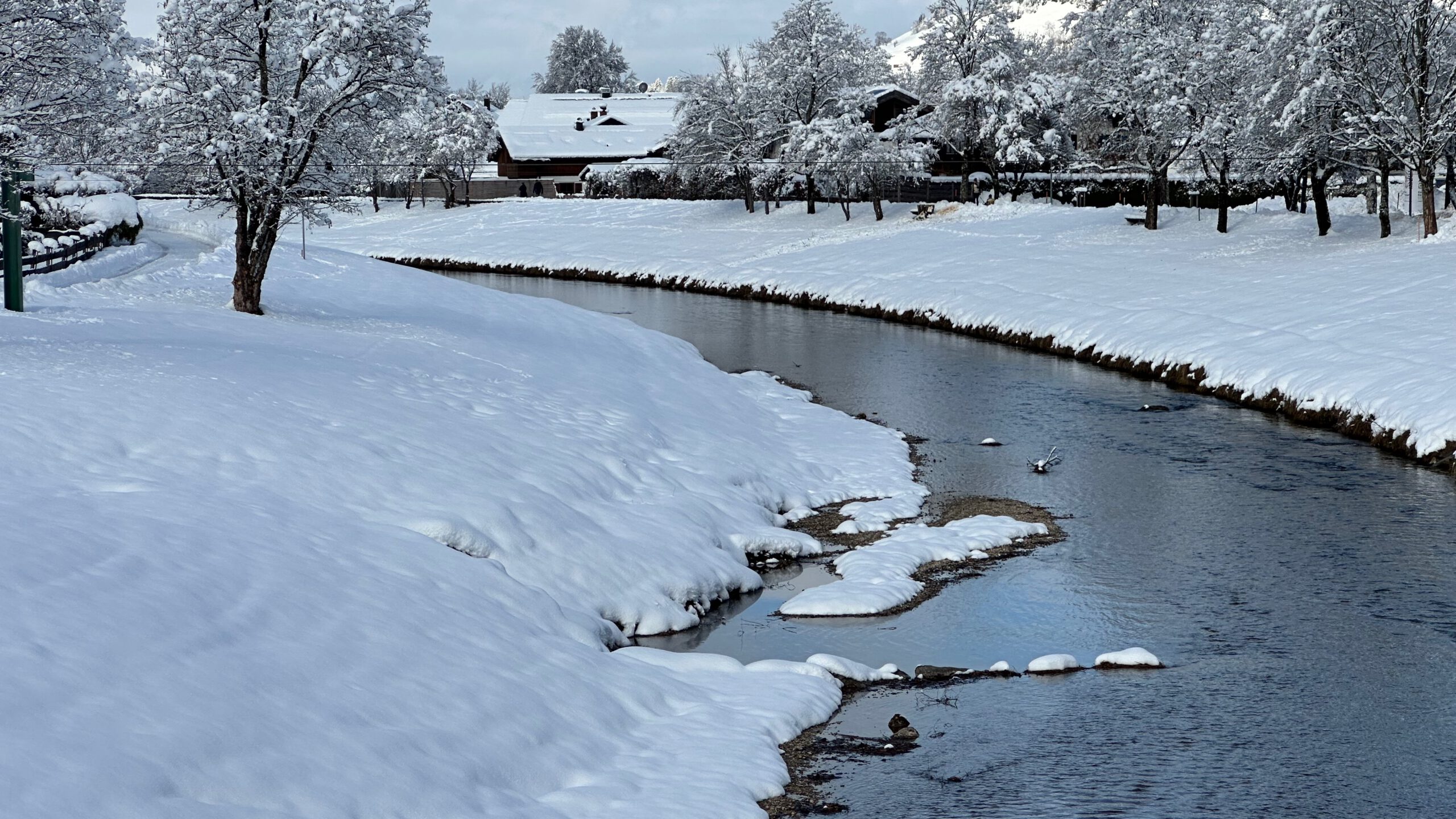 Schneebedeckte Landschaft an der Ammer in Oberammergau mit ruhigem Flusslauf und verschneiten Bäumen.