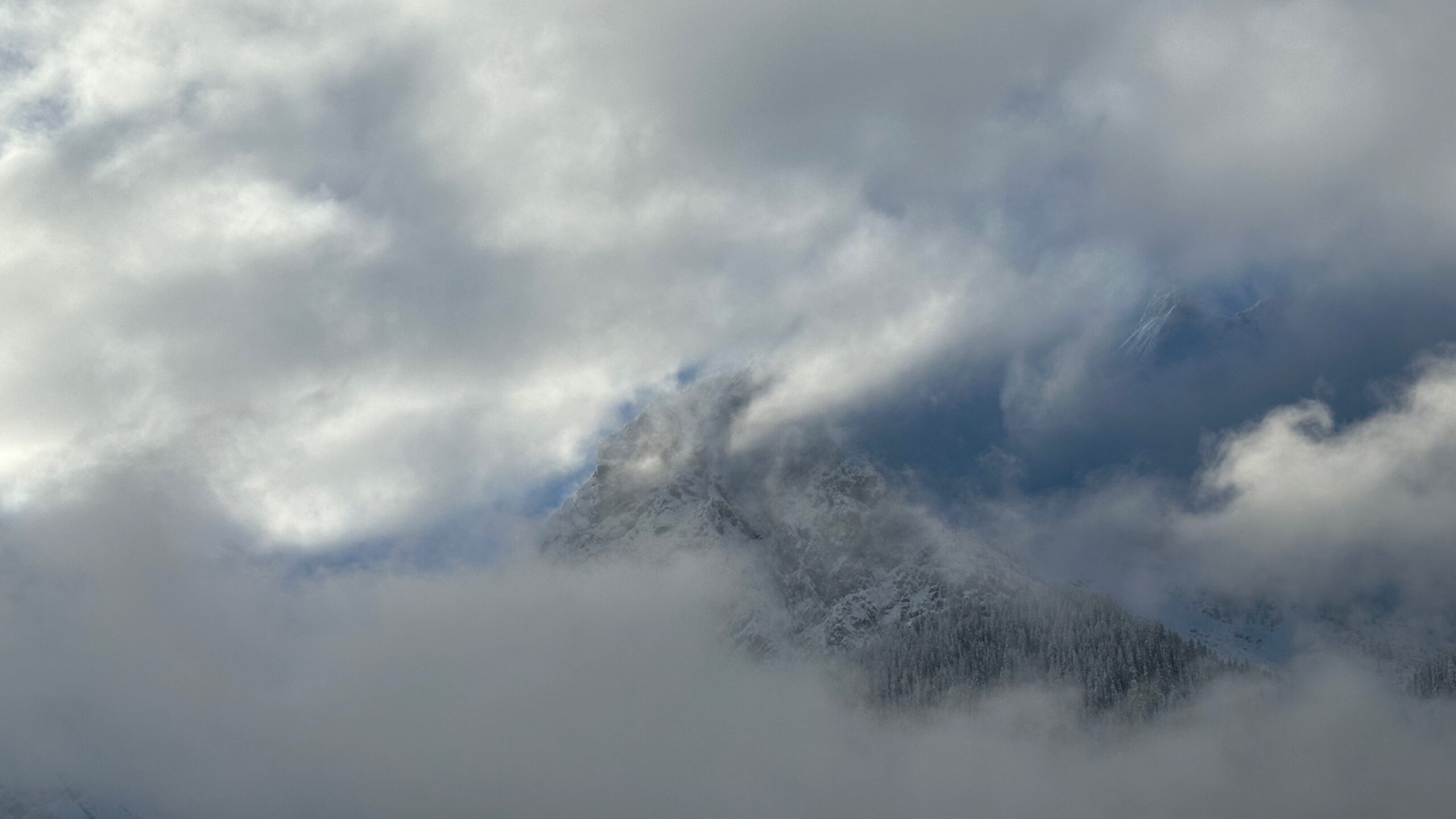 Verschneiter Berggipfel bei Oberammergau, der teilweise von dichten Wolken und Nebel verhüllt wird.